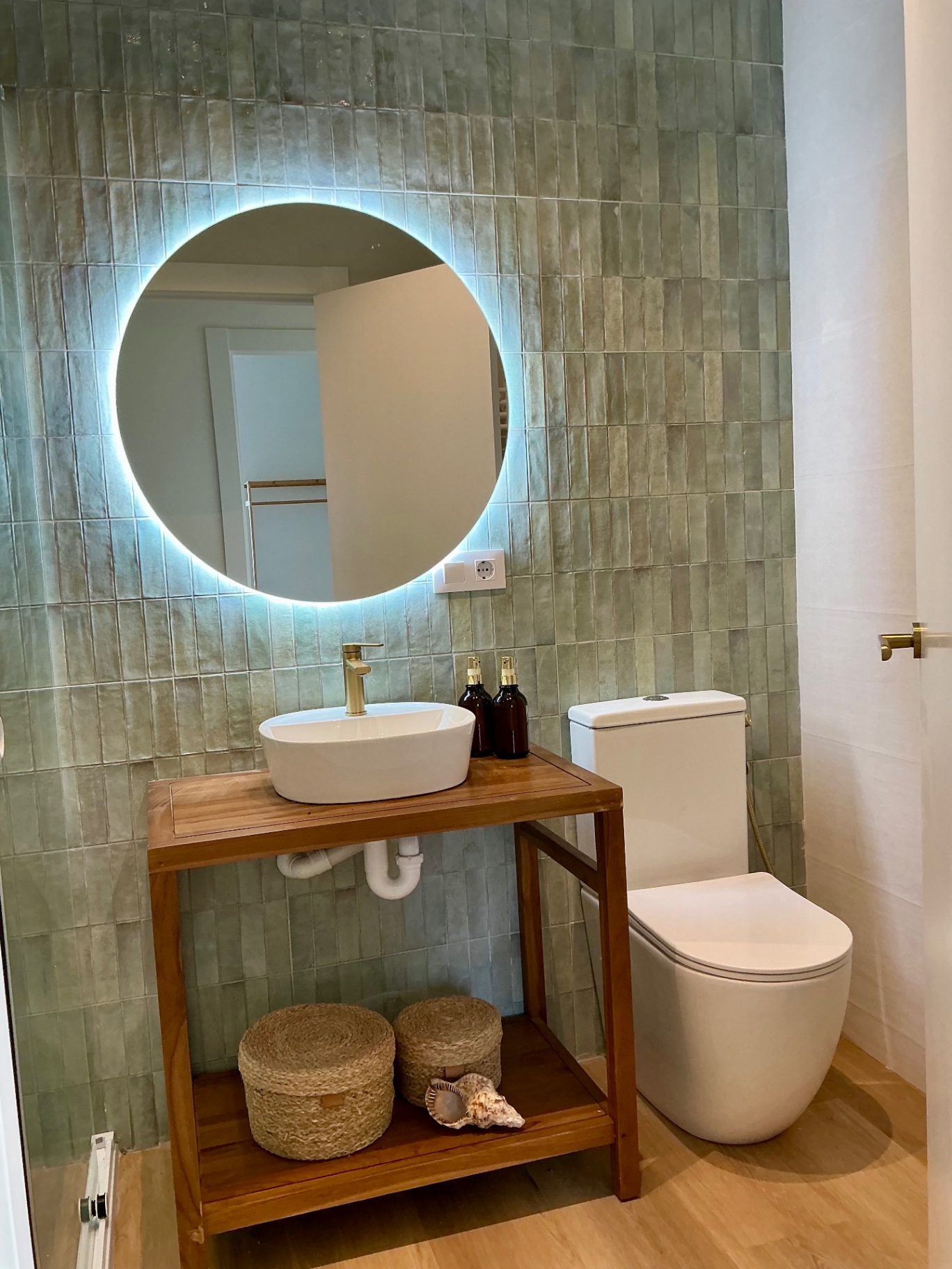 Baño con azulejo verde y lavabo sobre mueble de madera